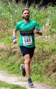 a masculine white person with a brown beard running in a race.