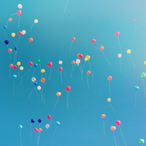 Many balloons floating in a blue sky