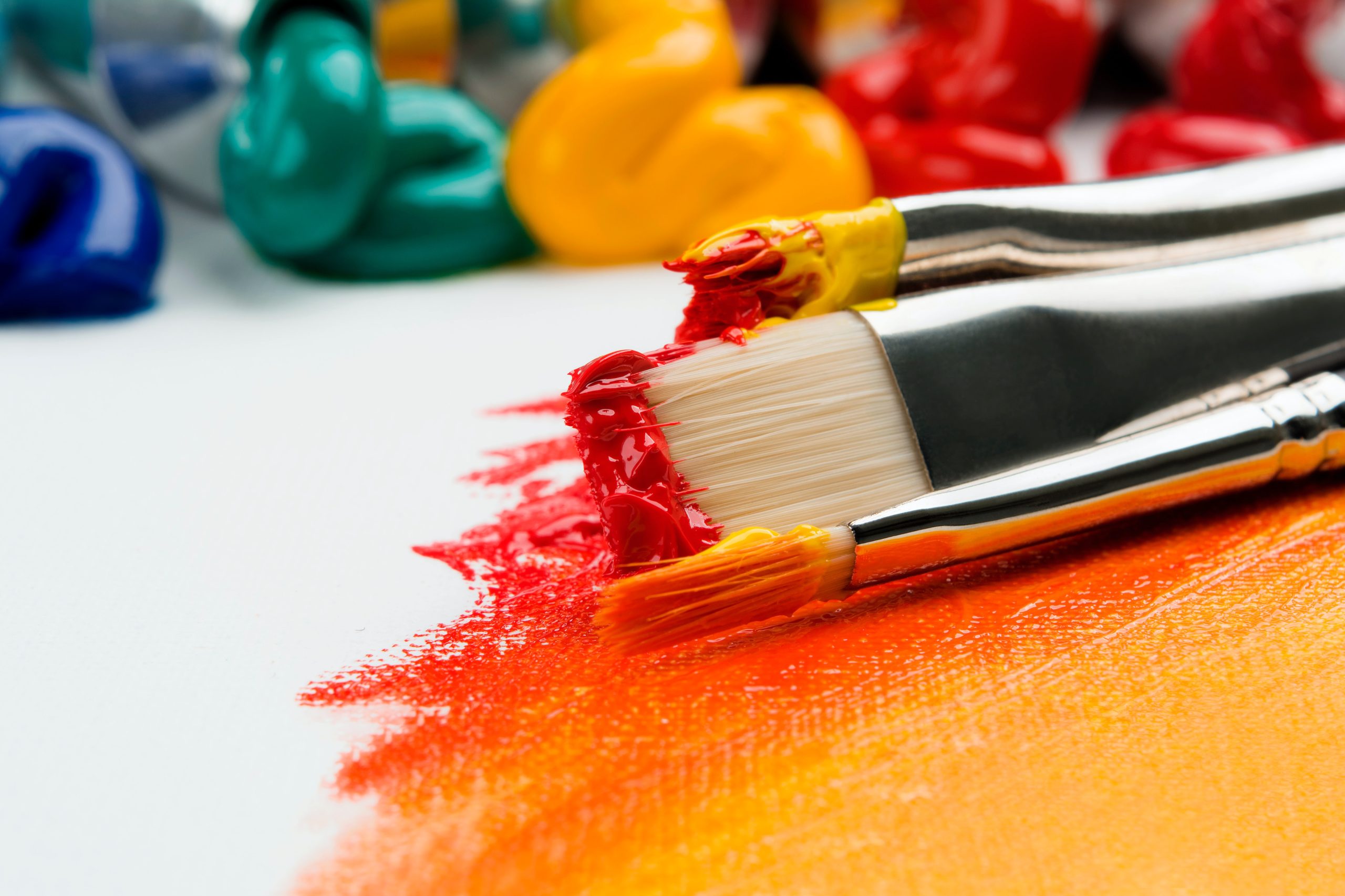 Paint brush with red and orange paint laid down on a table top